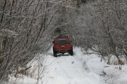2003 Jeep TJ - A red Jeep Wrangler TJ navigates a snow-covered path through a wooded area.