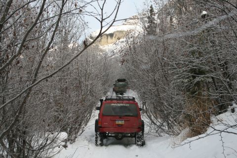 2003 Jeep TJ - Multiple Jeeps navigate a snowy path through a wooded area with mountains in the background.