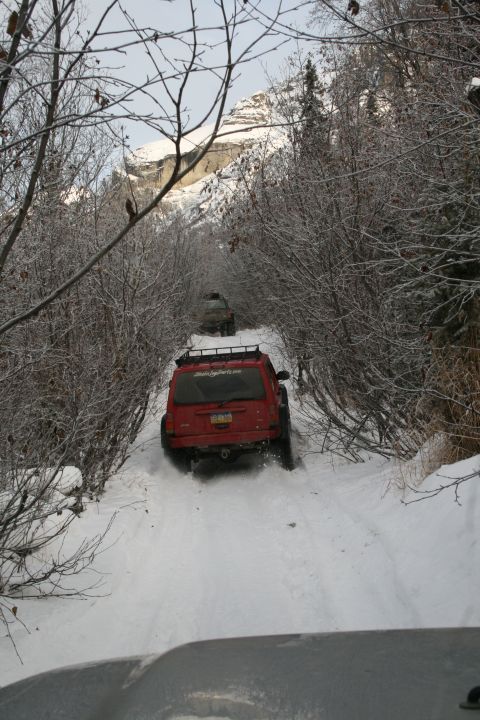 2003 Jeep TJ - A red SUV navigates a snow-covered trail, with another vehicle following closely behind.