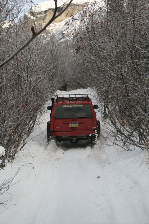 2003 Jeep TJ - A red Jeep Cherokee XJ navigates a snowy forest trail, with another vehicle ahead.