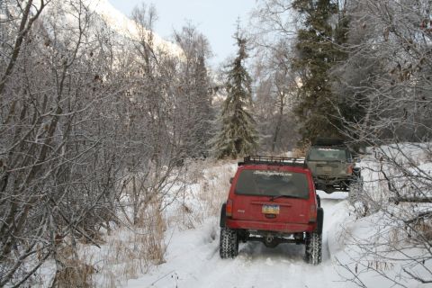 2003 Jeep TJ - Two Jeeps navigate a snow-covered trail through a winter forest.