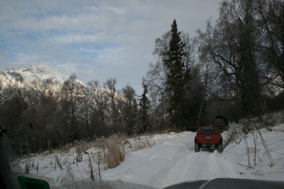 Several Jeeps driving on a snow-covered road with trees and a mountain in the background