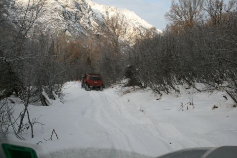 2003 Jeep TJ - A red SUV navigates a snow-covered road in a mountainous, wooded area.