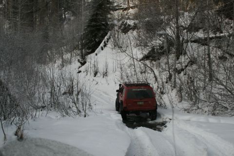2003 Jeep TJ - A red Jeep Cherokee navigates a snow-covered trail, its rear lights visible as it drives away.