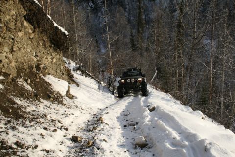 2003 Jeep TJ - A Jeep Wrangler navigates a snow-covered trail through a wooded mountainside.