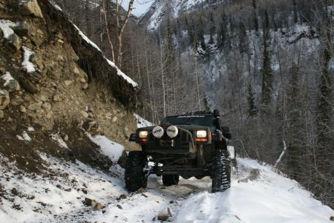 2003 Jeep TJ - Modified Jeep Cherokee XJ navigates a challenging snowy trail in a mountainous, wooded area.