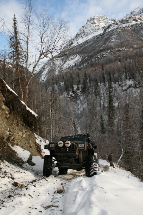 2003 Jeep TJ - A heavily modified Jeep Cherokee XJ navigates a snow-covered path in a mountainous, wooded area.