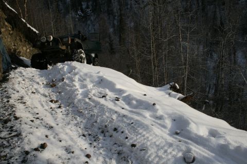 2003 Jeep TJ - A vehicle navigates a snow-covered mountain path with dense trees in the background.