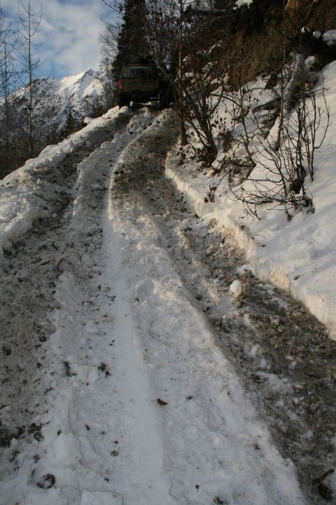 2003 Jeep TJ - A green Jeep Wrangler navigates a challenging snowy and muddy incline on a mountain trail.