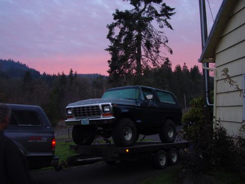 1979 Ford Bronco - A dark 1979 Ford Bronco is loaded onto a trailer as the sun sets, with another truck visible to the left.