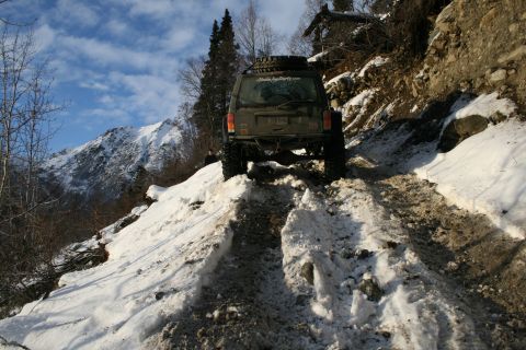 2003 Jeep TJ - A Jeep Cherokee XJ navigates a challenging snowy path on a steep mountain incline.