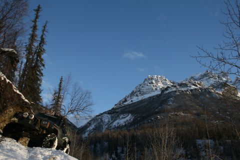 2003 Jeep TJ - A vehicle navigates a steep, snow-covered incline under a clear blue sky with mountains ahead.