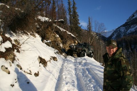 2003 Jeep TJ - A man stands on a snow-covered mountain road next to a Jeep Wrangler navigating the challenging terrain.