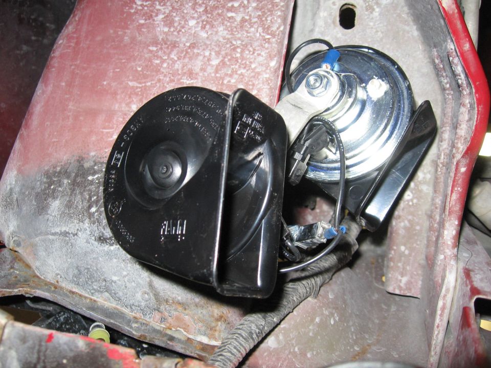 Two black and silver vehicle horns mounted on a red metal surface with wiring