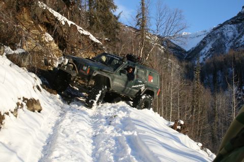 2003 Jeep TJ - Jeep Cherokee XJ navigates a steep, snow-covered mountain path during winter off-roading.