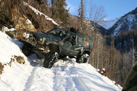 2003 Jeep TJ - A modified Jeep Cherokee XJ navigates a steep, snow-covered mountain path.