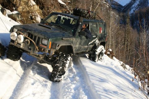 2003 Jeep TJ - A modified green Jeep Cherokee XJ navigates a steep, snow-covered mountain path, demonstrating its off-road capabilities.