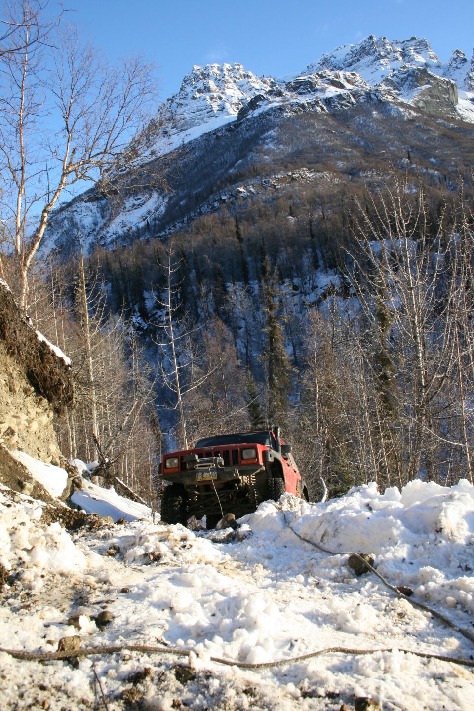 Red Jeep Cherokee on a snowy, wooded mountain trail with a winch cable attached