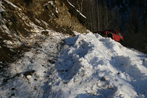 2003 Jeep TJ - A red 2003 Jeep TJ navigates a challenging snowy path on a steep mountainside.
