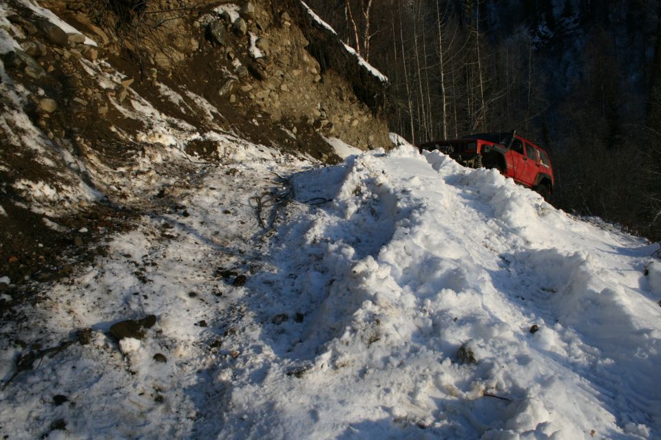 Red 2003 Jeep TJ climbing a steep, snow-covered trail next to a rocky embankment
