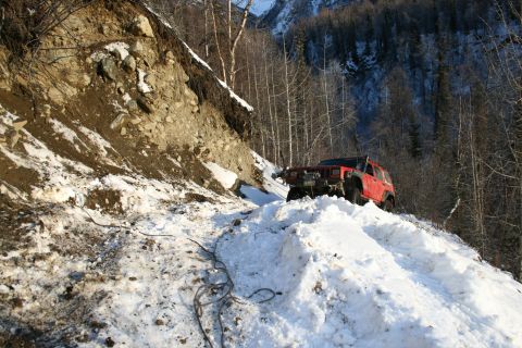 2003 Jeep TJ - Red Jeep Cherokee XJ navigates a challenging snowy mountain path, showing off its off-road capabilities.