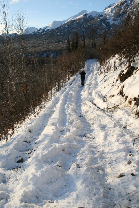 2003 Jeep TJ - A person walks up a snow-covered mountain road, leaving tracks behind them.