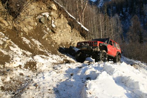 2003 Jeep TJ - A red Jeep Cherokee XJ navigates a challenging snowy mountain path, demonstrating its off-road capabilities.