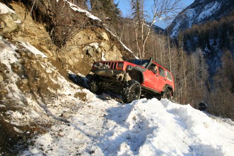2003 Jeep TJ - A red Jeep Cherokee navigates a challenging snowy incline, its off-road capabilities.