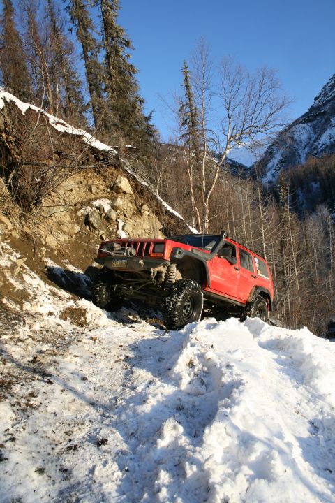 2003 Jeep TJ - Jeep Cherokee XJ navigates a challenging snowy and muddy trail in a mountainous area.