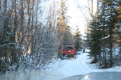 2003 Jeep TJ - A red 2003 Jeep TJ navigates a snow-covered trail surrounded by trees.