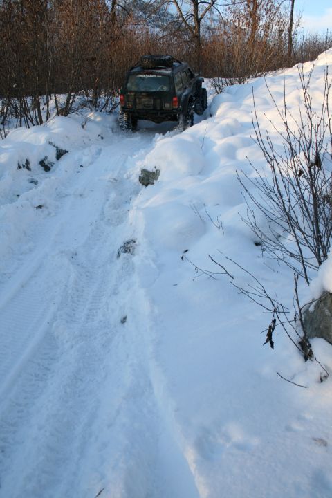 2003 Jeep TJ - A Jeep Cherokee XJ navigates a snow-covered trail, its tires kicking up snow as it climbs.