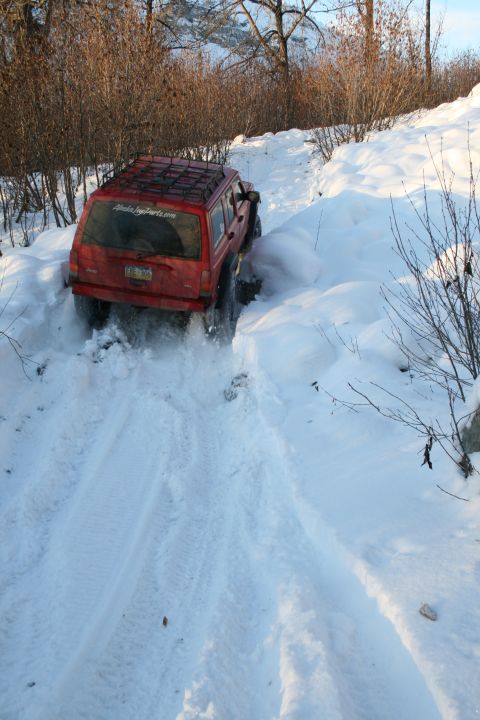 2003 Jeep TJ - A red Jeep Cherokee XJ navigates a snowy trail, kicking up snow as it goes.