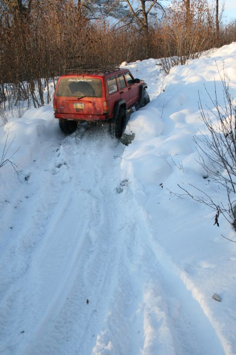 2003 Jeep TJ - Red Jeep Cherokee XJ navigates a challenging snowy incline, its tires churning through the snow.