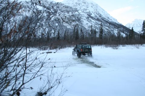 2003 Jeep TJ - SUV navigates a snowy path with a mountain range behind it.
