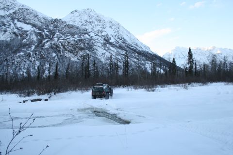 2003 Jeep TJ - A dark SUV navigates a snowy landscape with snow-capped mountains in the background.