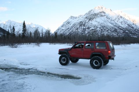 2003 Jeep TJ - A red Jeep Cherokee XJ navigates a snowy landscape with snow-capped mountains behind it.