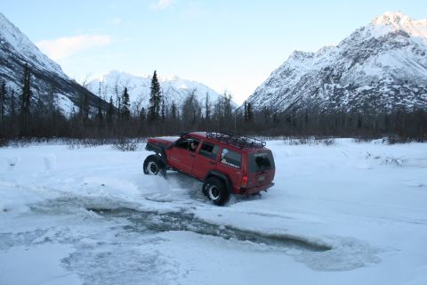 2003 Jeep TJ - Red Jeep Cherokee navigates a snowy, icy terrain with a backdrop of snow-covered mountains.