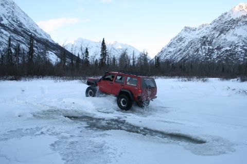 2003 Jeep TJ - Red Jeep Cherokee XJ navigates a snowy trail with mountainous terrain behind it.