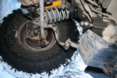 2003 Jeep TJ - Close-up of the front suspension and tire of a 2003 Jeep TJ, partially covered in snow.