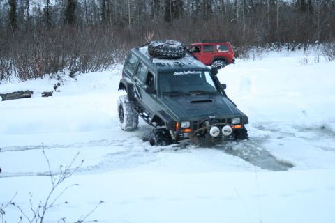 2003 Jeep TJ - Two Jeep Cherokee XJs navigate a snowy, icy terrain. The lead vehicle has a snorkel and spare tire on the roof.