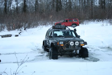 2003 Jeep TJ - Two modified Jeep Cherokees navigate a snowy trail, one with a roof-mounted spare tire and extra lights.