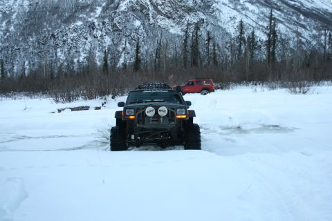 2003 Jeep TJ - A modified Jeep Cherokee XJ navigates a snowy landscape, with a red SUV visible in the distance.