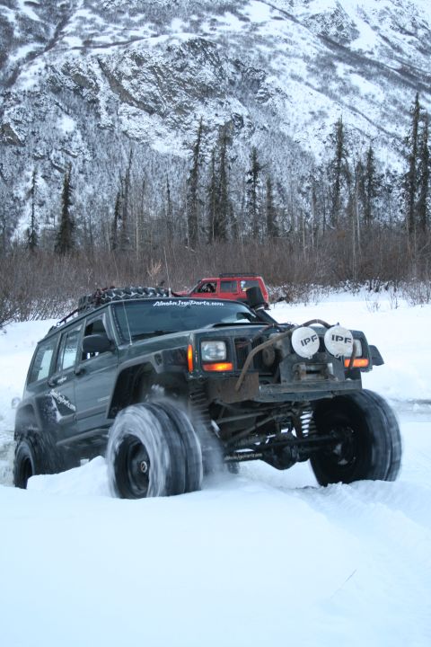 2003 Jeep TJ - A dark green Jeep Cherokee XJ navigates through a snowy landscape with another red Jeep in the background.