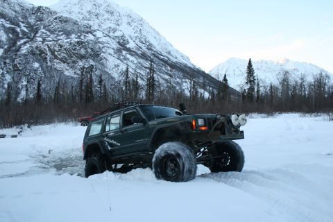 2003 Jeep TJ - Modified Jeep Cherokee XJ navigates a snowy landscape with snow-covered mountains in the distance.