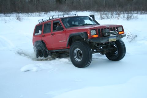 2003 Jeep TJ - This red Jeep Cherokee XJ is equipped for off-road conditions, navigating through a snowy landscape.