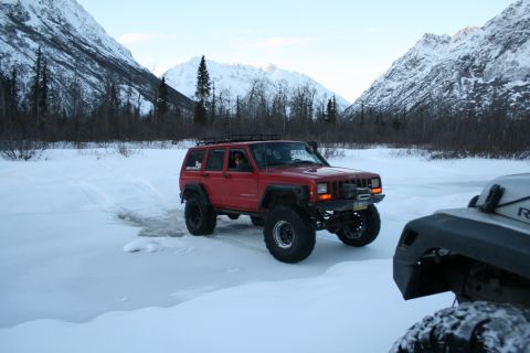 2003 Jeep TJ - A red Jeep Cherokee XJ navigates a snowy landscape with snow-covered mountains in the distance.
