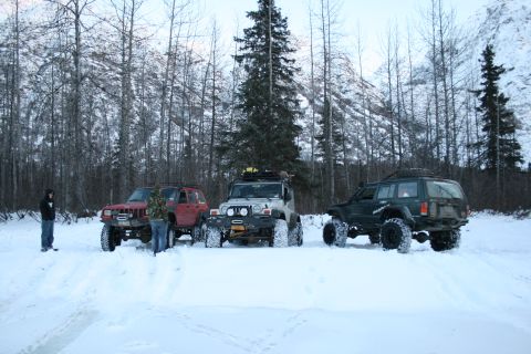 2003 Jeep TJ - Three modified Jeeps, including a silver 2003 Jeep TJ, are parked in a snowy landscape with trees and mountains in the background.