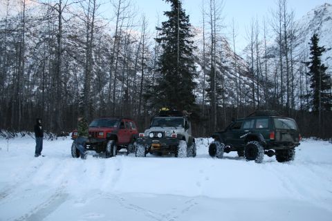 2003 Jeep TJ - Three modified Jeeps are parked in a snowy forest scene with mountains visible.