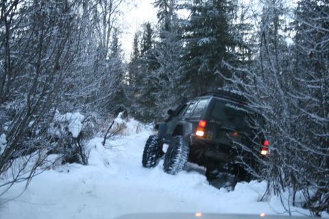 2003 Jeep TJ - A black SUV navigates a snowy trail, its large tires digging into the snow-covered ground.