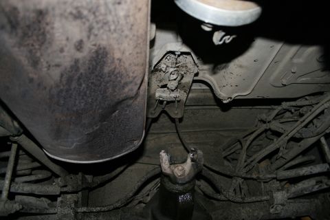 2003 Jeep TJ - The undercarriage of a vehicle shows the exhaust system and drivetrain components, covered in dirt and grime.